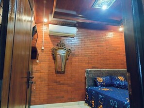 Una stanza con parete in mattoni, un letto con copriletto decorato, un condizionatore d'aria e uno specchio ornamentale.
