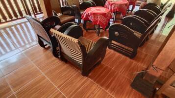 A restaurant interior with wooden chairs and tables, tiled flooring, and a decorative wall.