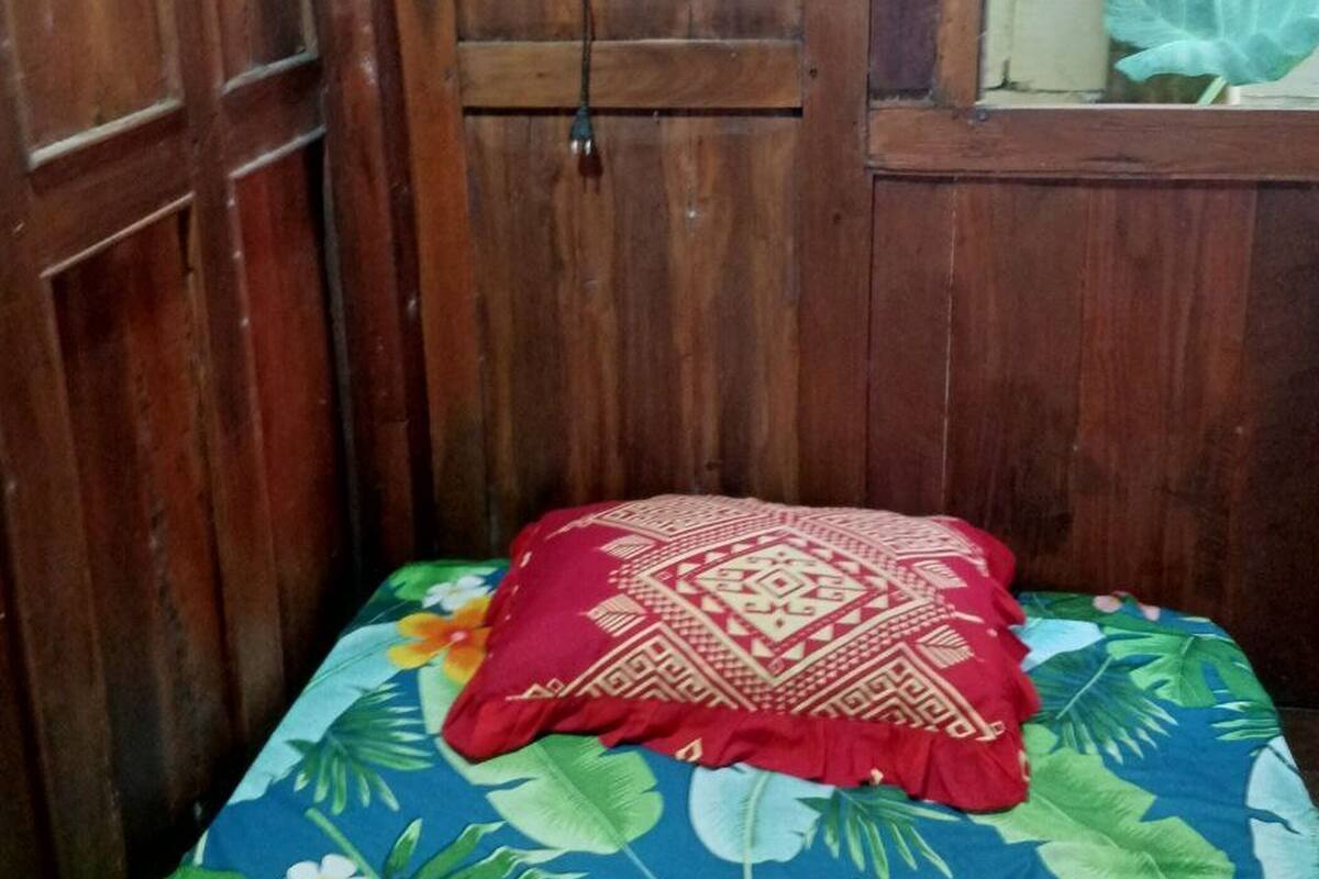 Een kleine kamer met een houten deur, een aan de muur bevestigde televisie en een bed met een bloemenprint sprei en een rood kussen.