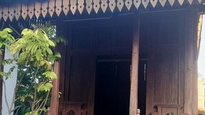 Une structure en bois avec un toit recouvert de tuiles, un banc en bois et un vélo à l’intérieur.