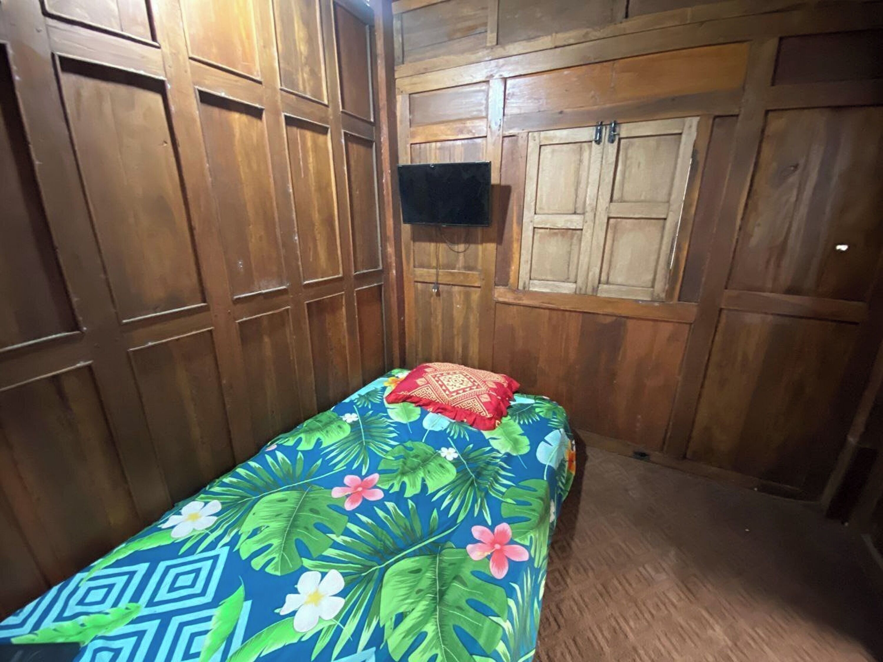 Una habitación pequeña con paneles de madera, una cama individual con colcha estampada y un televisor montado en la pared.