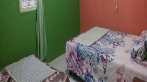 Una habitació petita amb un llit individual, una finestra amb cortina i un ventilador fixat a la paret.