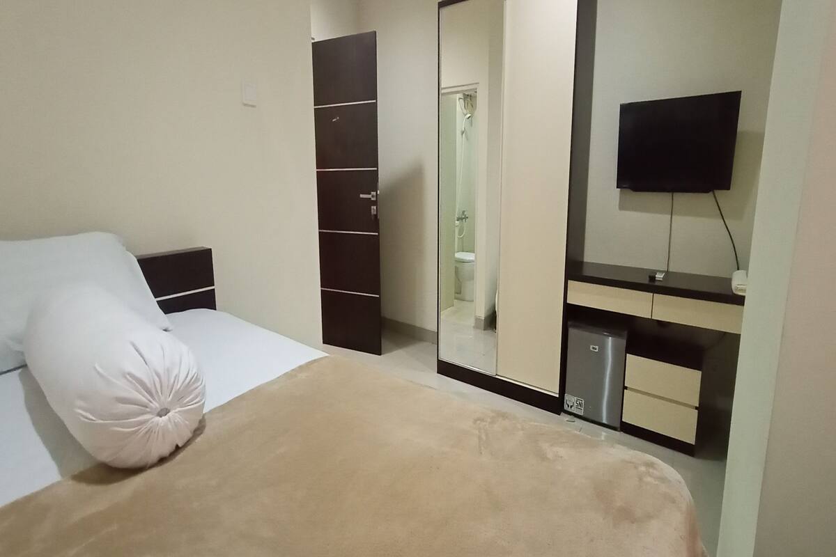 A bedroom with a bed, a wardrobe, a mirror, and a television.