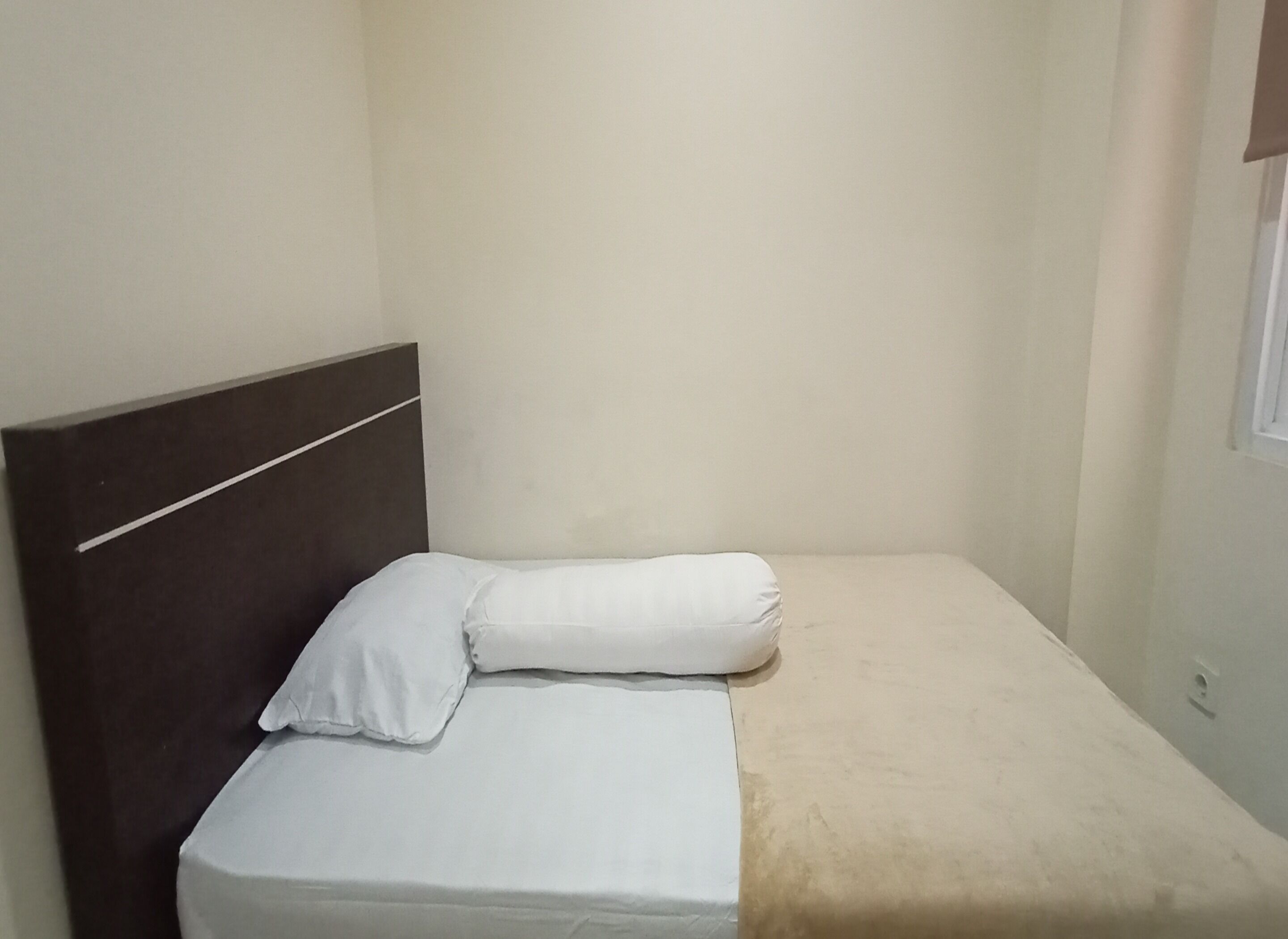 A small, single-bed room with a plain headboard and a beige mattress.