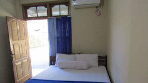 A bedroom with a bed, a blue bedspread, white pillows, a wooden headboard, a window with curtains, and an air conditioning unit on the wall. - Hotel Family Syariah 1 (Parangtritis)