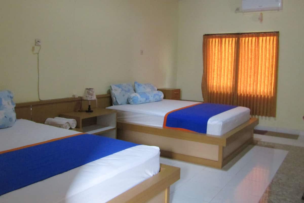 A hotel room with two beds, a nightstand, a lamp, and a window with curtains.