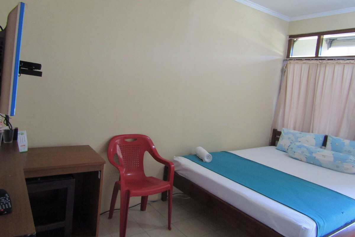 A small, simple room with a bed, a desk, and a red chair.