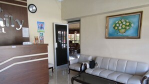 A reception area with a wooden reception desk, a beige sofa, a glass coffee table, and a painting of flowers on the wall. - Hotel Family Syariah 1 (Parangtritis)