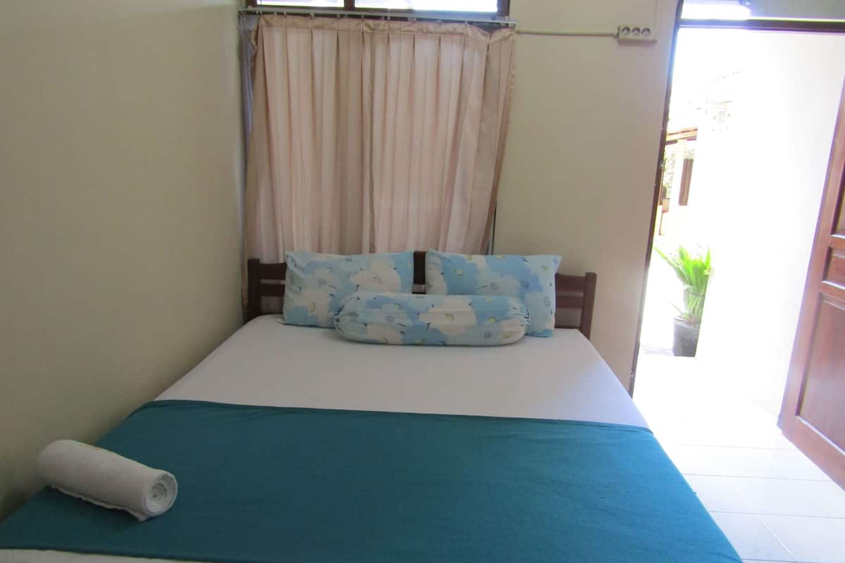 A small bed with a blue bedspread, two pillows with a cloud pattern, and a rolled towel on the side.