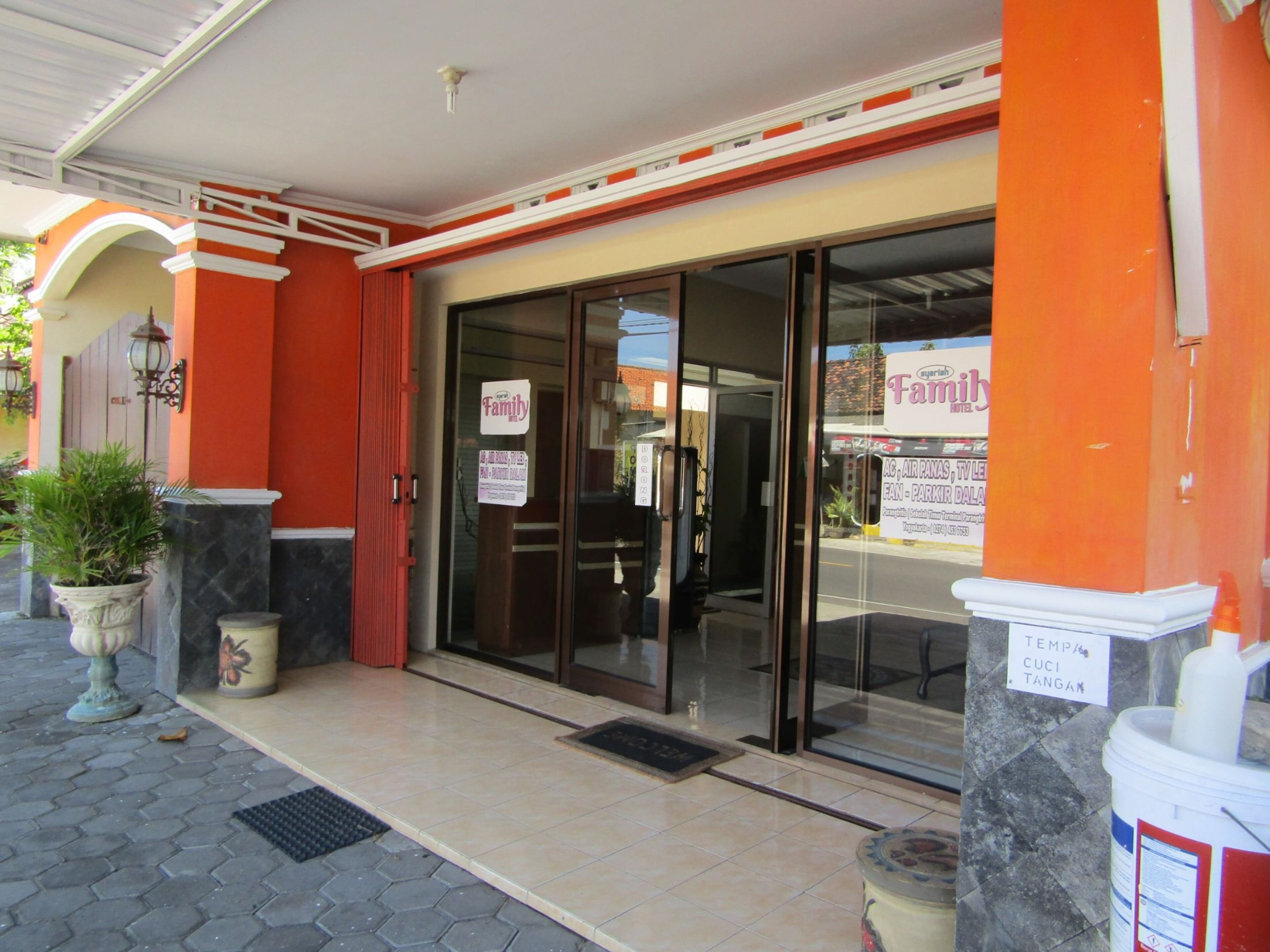 A building entrance with a glass door, a sign reading "Family", and a sign indicating "Temp/Cuci Tangan" (temporary/cleaning area).