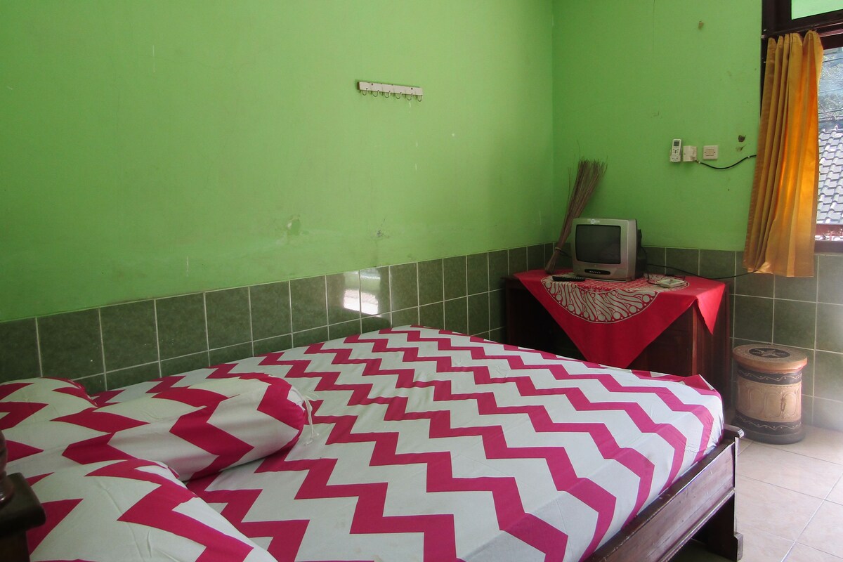 A room with a bed, a small table with a television, and a window with curtains.