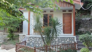 A small house with a stone foundation, a wooden door, and a red roof.