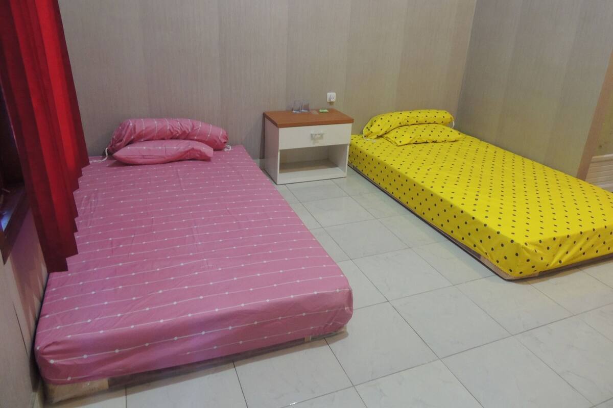 A bedroom with two beds, one with a pink mattress and the other with a yellow mattress.