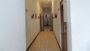A hallway with a tiled floor, doors on the right, and potted plants on the walls.