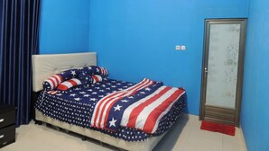 A bedroom with a bed covered in an American flag-themed blanket, a blue wall, an air conditioning unit, a wardrobe, and a red rug.
