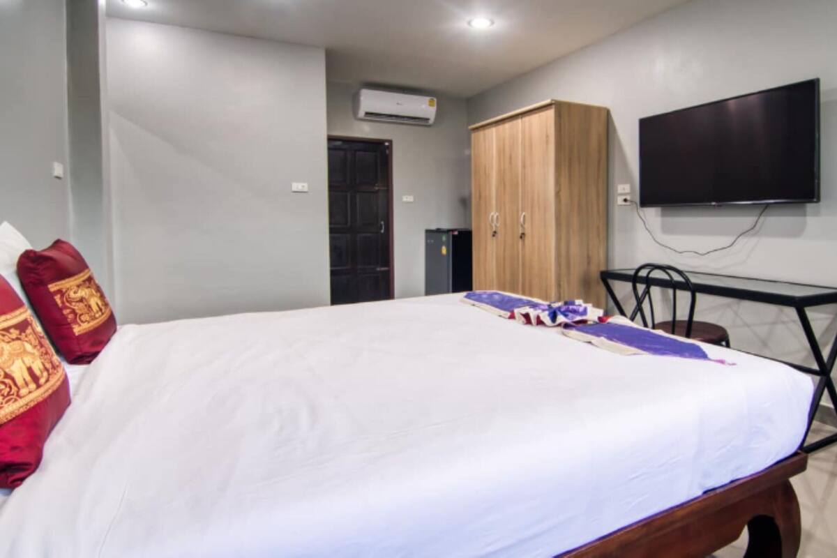 A bedroom with a bed, a wardrobe, a television, and a desk.