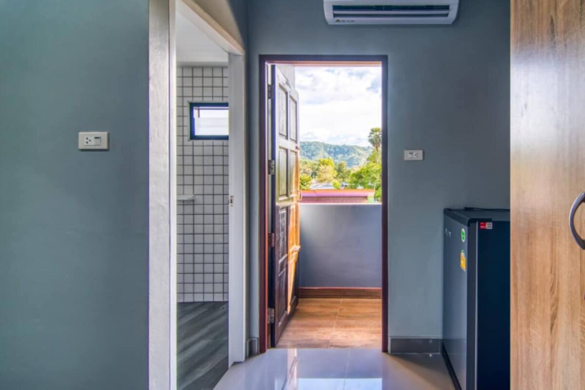 A narrow hallway leading to a balcony with a view of greenery and hills.