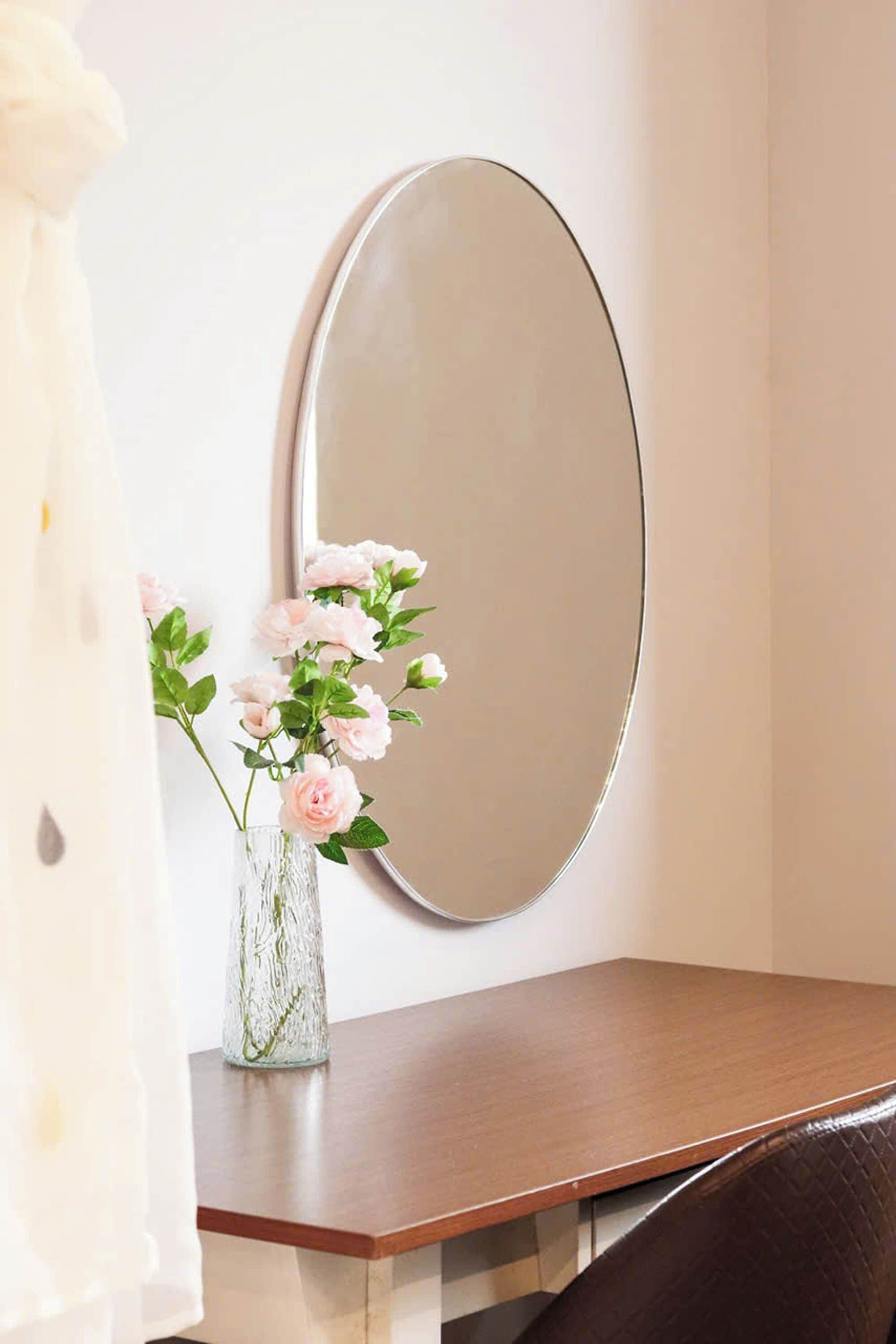 A room with a wooden desk, a glass vase with flowers, and a large mirror on the wall.