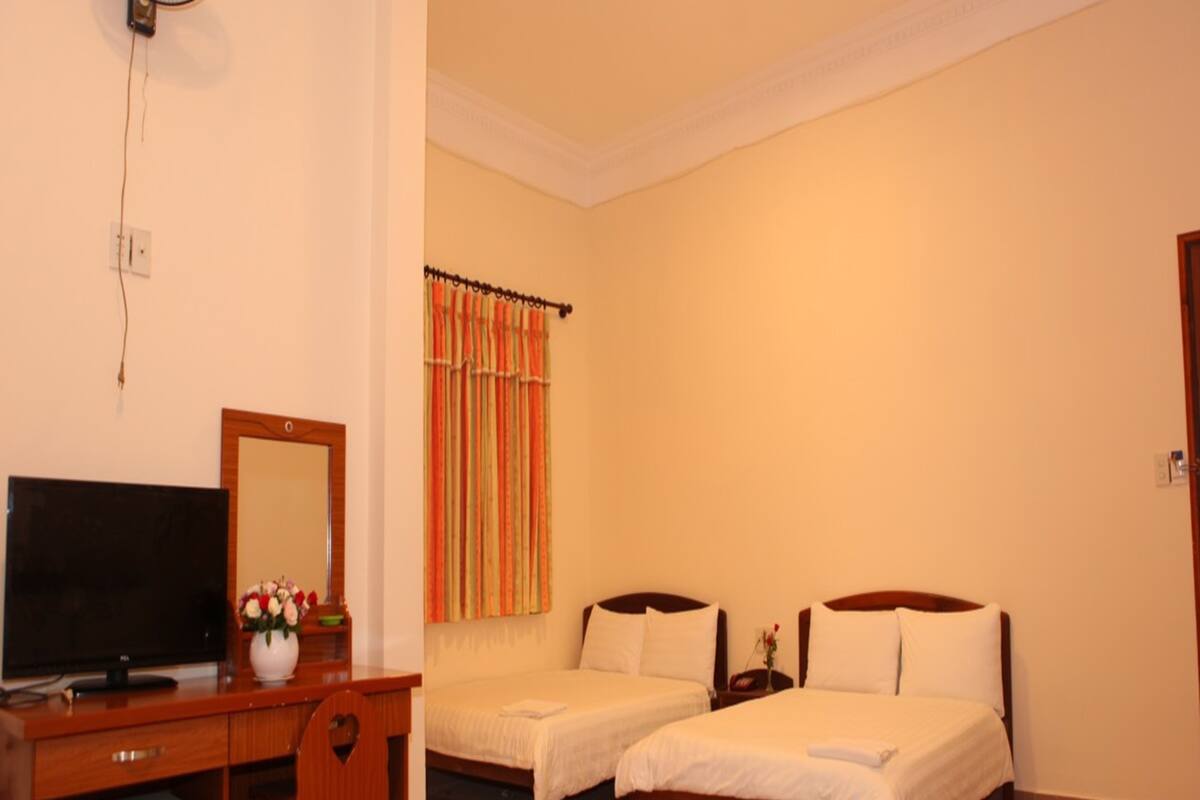 Une chambre d’hôtel avec deux lits simples, un bureau avec une télévision et un petit réfrigérateur.