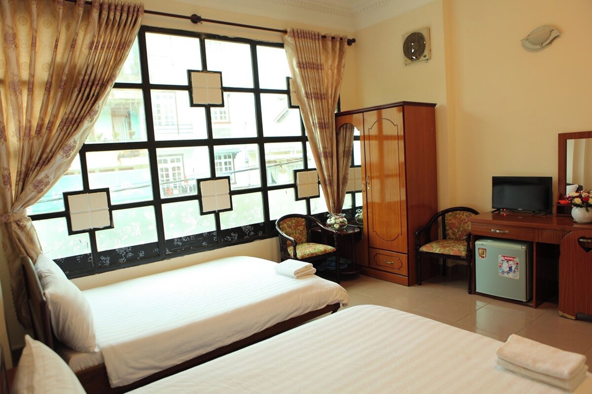 A hotel room with a bed, a desk with a television, a refrigerator, and a chair.