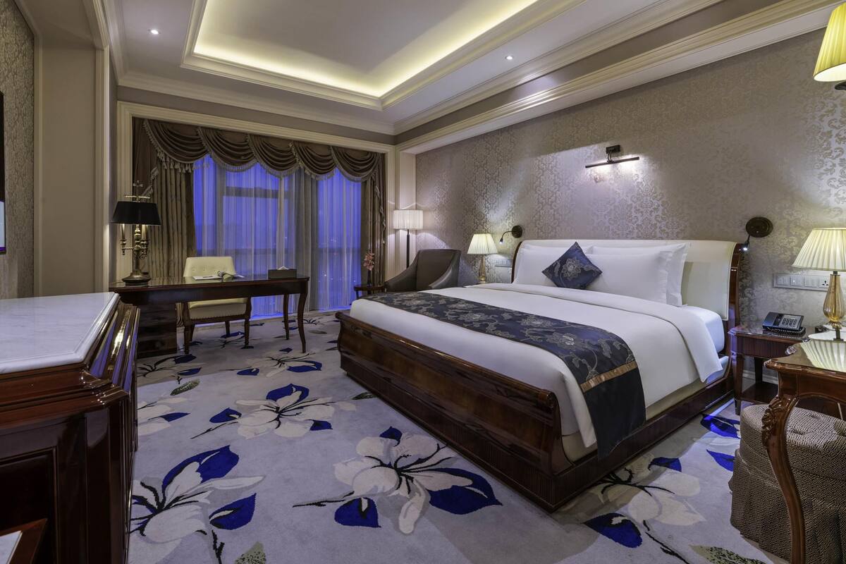 Habitación de hotel con una cama grande, un escritorio, una silla y vistas a la ciudad desde la ventana.