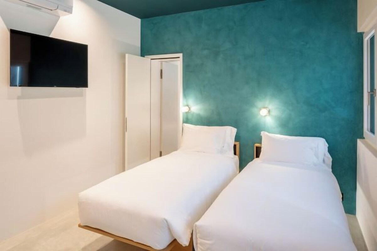 A bedroom with two single beds, a TV mounted on the wall, and a teal-colored wall.
