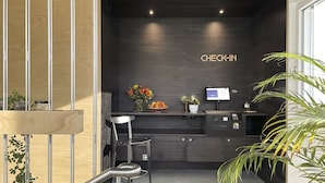 A modern reception desk with a 'CHECK-IN' sign, a computer monitor, and a vase with flowers. - Riva Rooms & Studios (Minusio)