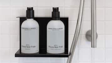 Two bottles of Marie-Stella-Maris products on a black shelf in a bathroom with white tiles.