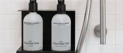 Dos botellas de productos Marie-Stella-Maris sobre una repisa negra en un baño con azulejos blancos.