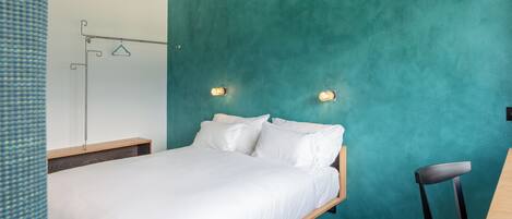 Quarto com parede azul-turquesa, estrutura de cama de madeira, roupa de cama branca e duas luminárias fixadas na parede.