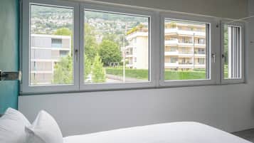 Une chambre avec une grande fenêtre, un lit et une vue sur un quartier résidentiel.