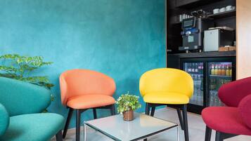 A seating area with colorful chairs and a small table, a refrigerator with beverages, and a coffee machine.