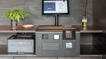 En receptionsdisk med en Brother-skrivare, en krukväxt, ett litet bord med en skål och en digital skärm som visar alternativen "Incheckning" och "Utcheckning".
