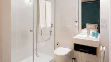 Et moderne badeværelse med en glasvægs brusekabine, toilet og et spejl med vask.