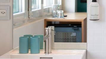 Une salle de bain avec un lavabo, un miroir et un flacon de gel pour les mains et le corps fixé au mur.