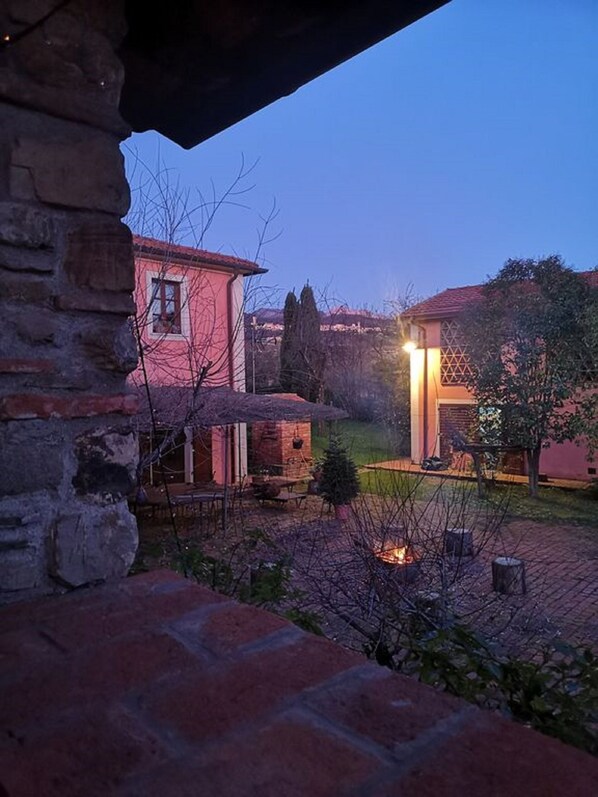 A courtyard with a stone wall, a small wooden structure, and a building with a red roof. - Il Fienile -The Barn at Rose Cottage in Tuscany (Caniparola Fosdinovo,)