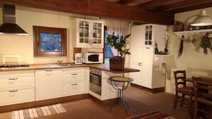 A compact kitchen with white cabinetry, a microwave, a stove, and a small dining area with a table and chairs. - Il Fienile -The Barn at Rose Cottage in Tuscany (Caniparola Fosdinovo,)