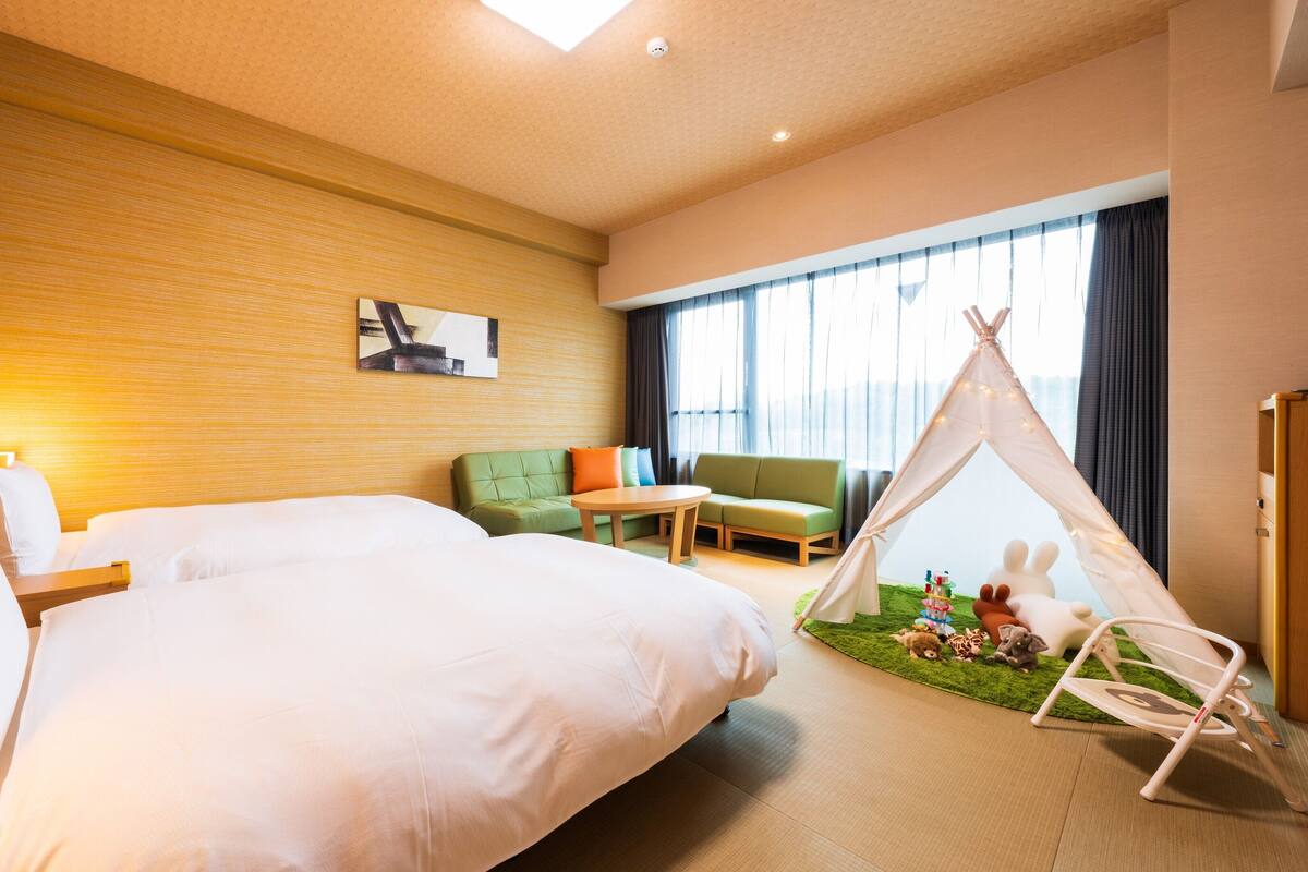 A hotel room with a large bed, a green sofa, a small table, a teepee, and a wall with animal stickers.