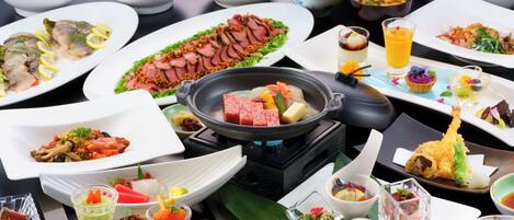 Una variedad de platos y bebidas sobre una mesa, incluyendo un caldo caliente, sushi y un vaso de jugo de naranja.