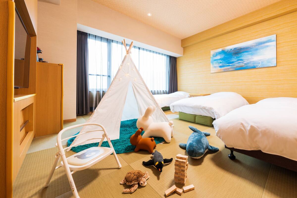 A hotel room with two beds, a play tent, a crib, and various toys.