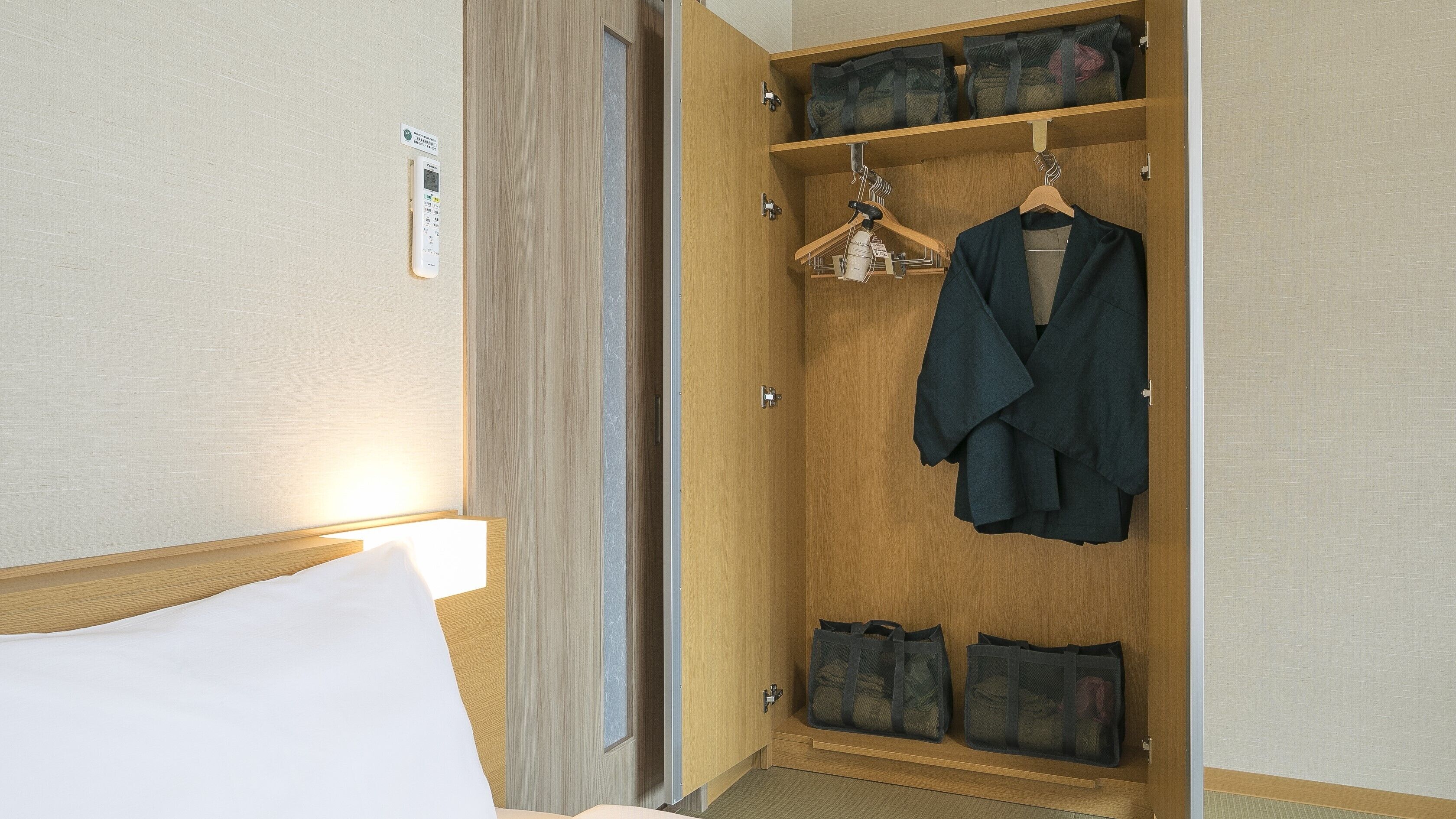 A hotel room with a wooden wardrobe, a bed with white linens, and a bedside table.