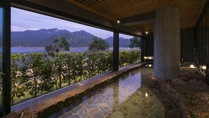 Un interior moderno con piscina revestida de piedra, vista a montañas y un lago, y techo de madera.