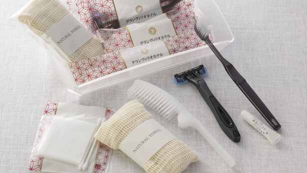 Une collection d’articles de toilette comprenant une serviette en tissu naturel, un peigne, un rasoir et une brosse à dents, le tout disposé sur une surface en tissu texturé.