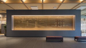 Un área de recepción con una obra de arte grande y montada en la pared que representa arquitectura tradicional, un banco y una planta en maceta.