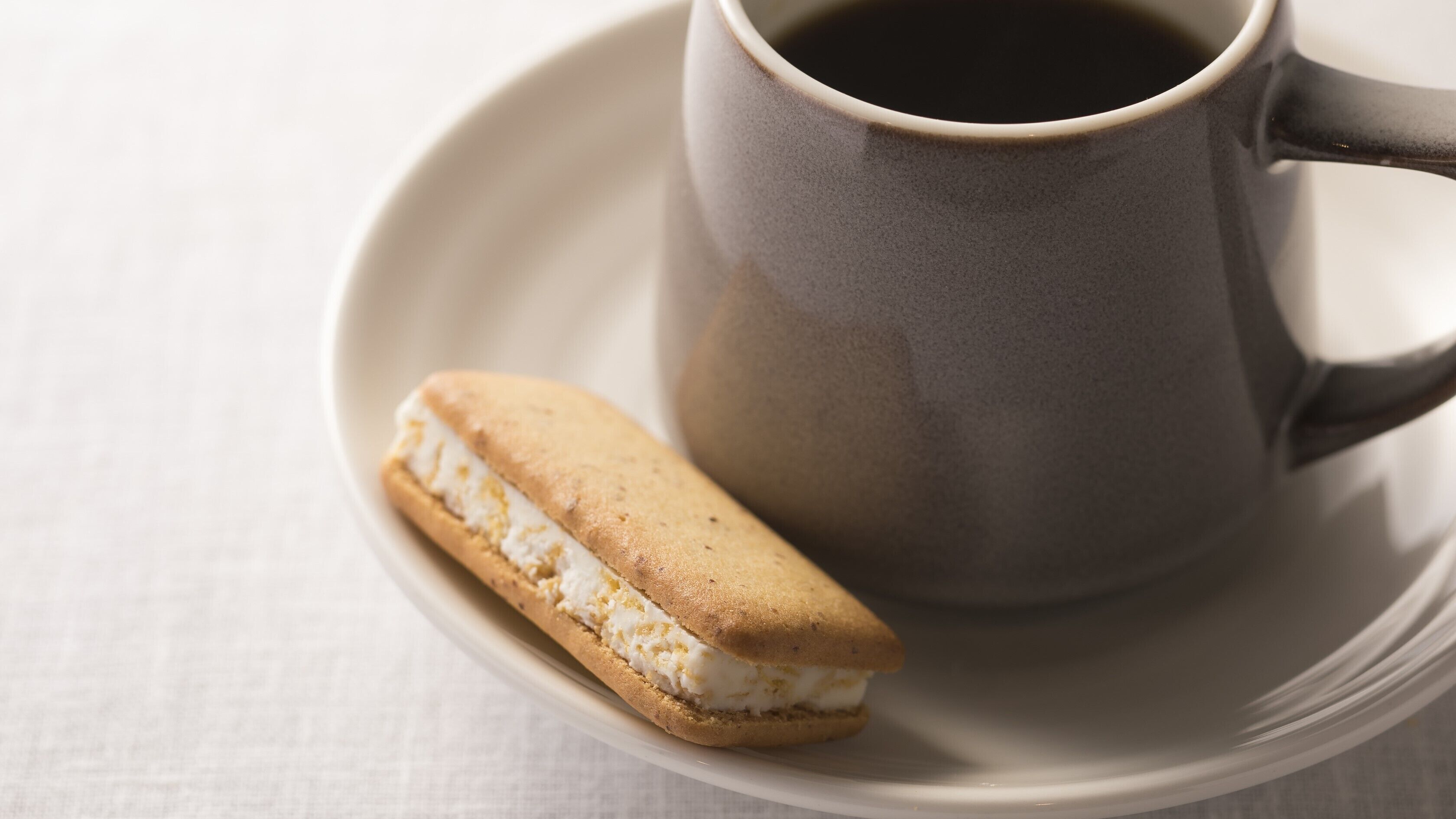 Una taza de café sobre un platito con un sándwich.