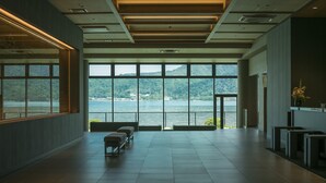 Un vestíbulo amplio con un gran ventanal que ofrece vistas a un lago y colinas. Hay bancos y un mostrador de recepción.