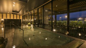 Un área de piscina interior moderna con paredes de vidrio, suelo mojado y vistas al exterior.