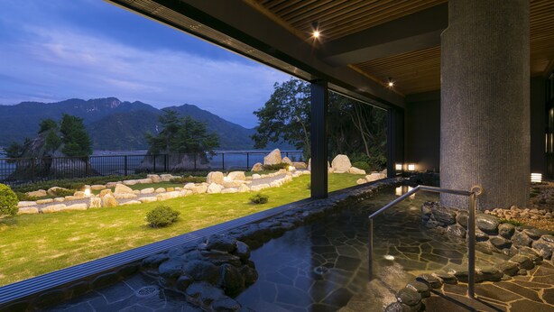 Zona de piscina moderna al aire libre con vistas a montañas y un lago.