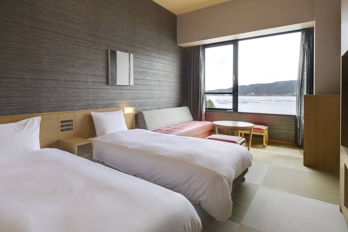 A hotel room with two beds, a small table, and a view of the sea.