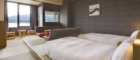 A modern hotel room with a large bed, a seating area with a sofa and chairs, a small table, and a large window offering a view of the mountains.